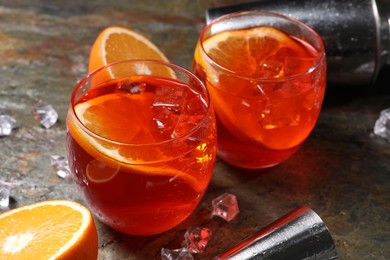 Aperol spritz cocktail, ice cubes and orange slices in glasses on grey textured table, closeup