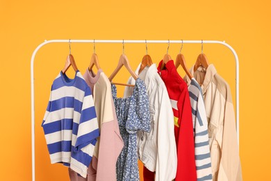 Photo of Rack with stylish women's clothes on wooden hangers against orange background