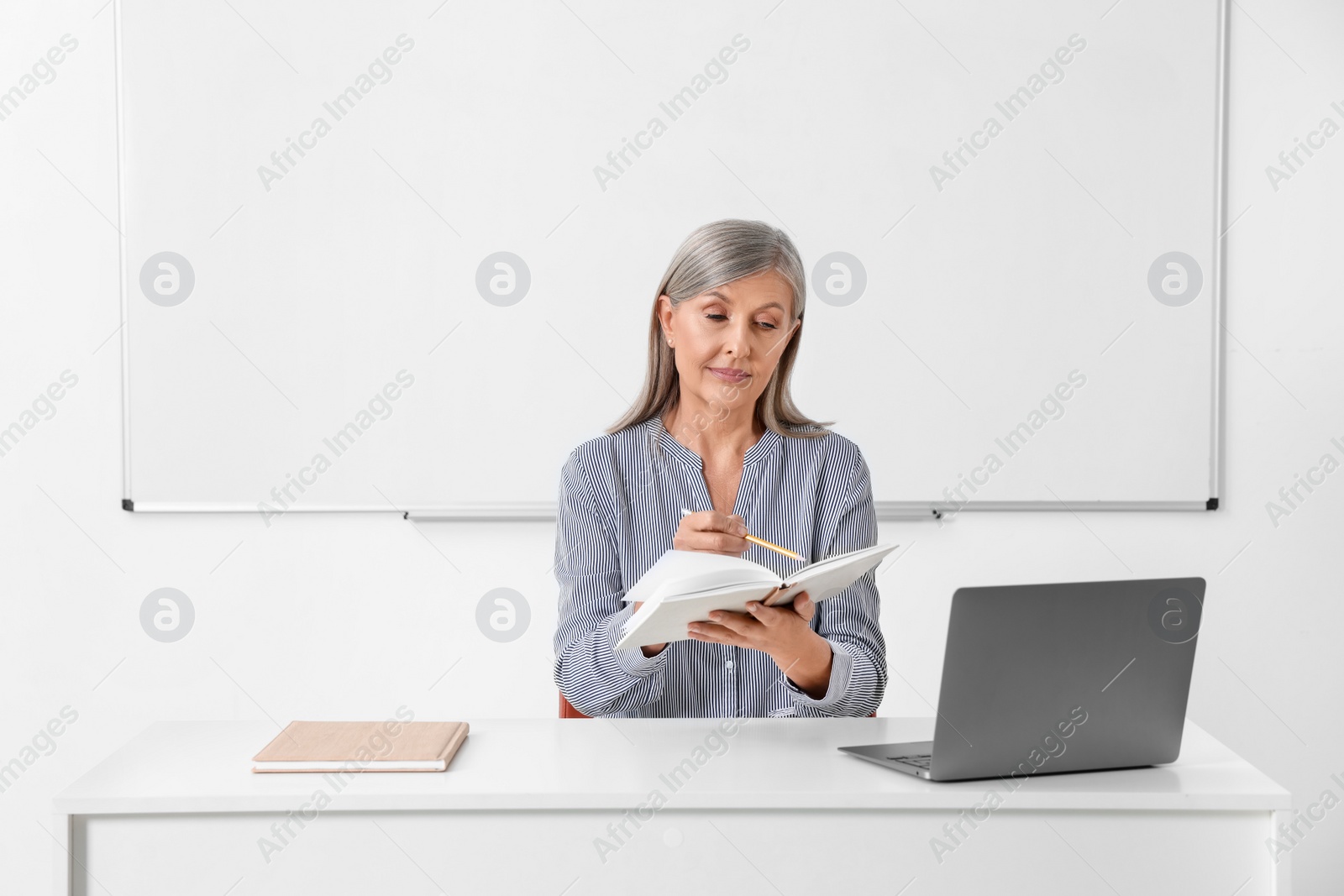 Photo of Professor giving lecture near laptop at desk in classroom