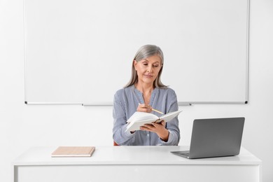 Professor giving lecture near laptop at desk in classroom