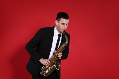 Photo of Young man in elegant suit playing saxophone on red background