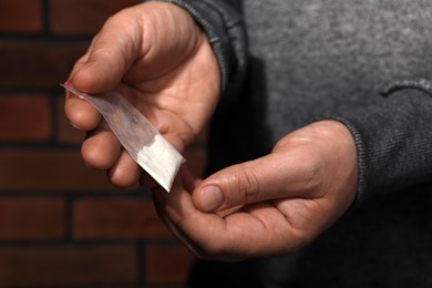 Drug addiction. Man with plastic bag of cocaine on blurred background, closeup
