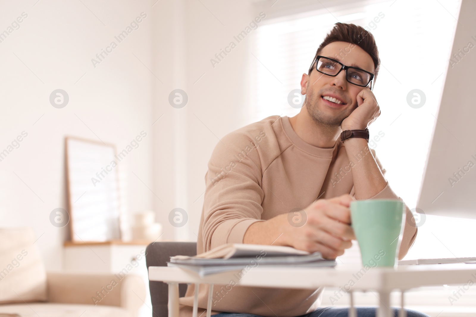 Photo of Young man with cup of drink relaxing at table in office during break