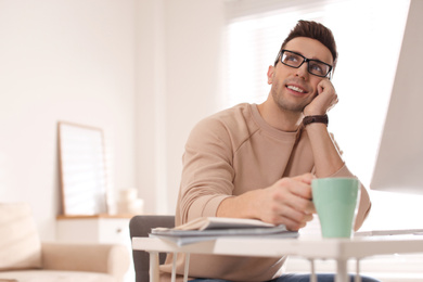 Young man with cup of drink relaxing at table in office during break