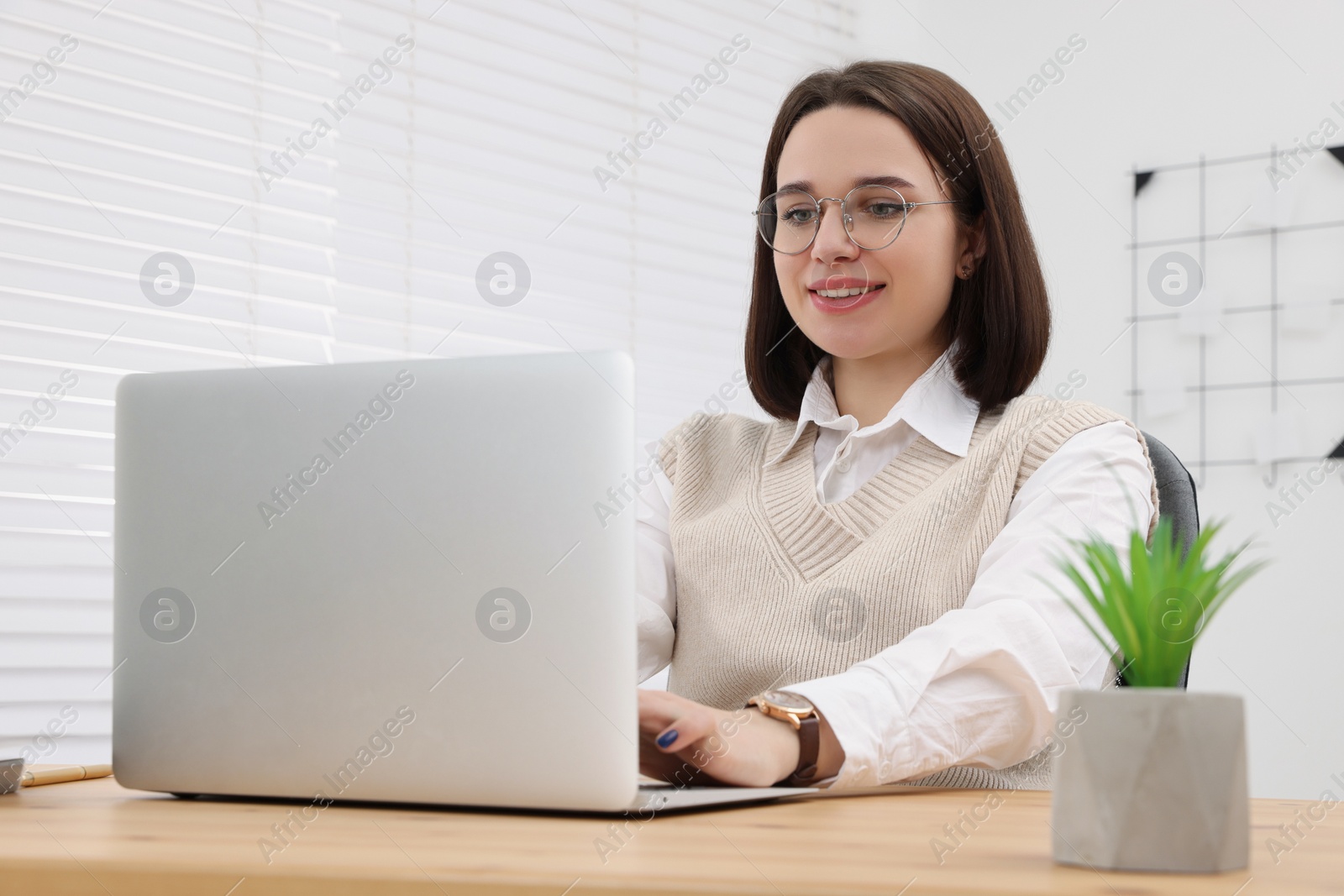 Photo of Happy young intern working with laptop at table in modern office