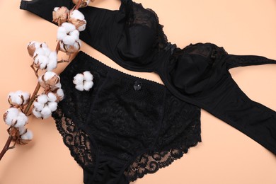 Photo of Elegant black plus size women's underwear and fluffy cotton flowers on beige background, flat lay