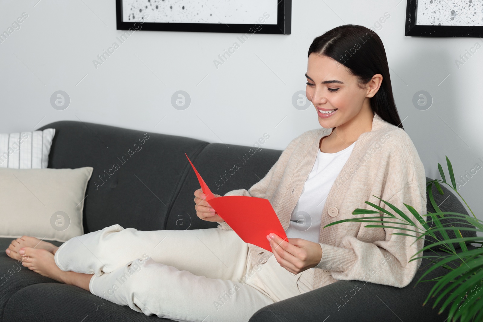 Photo of Happy woman reading greeting card on sofa in living room