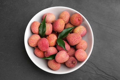Photo of Fresh ripe lychee fruits in white ceramic bowl on black table, top view
