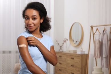 Photo of Young woman with adhesive bandage on her arm after vaccination indoors. Space for text