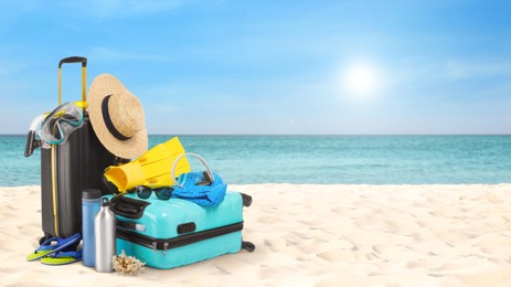 Image of Suitcases with beach accessories on sand near ocean, space for text