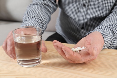 Photo of Senior man holding pills and glass of water at table, closeup