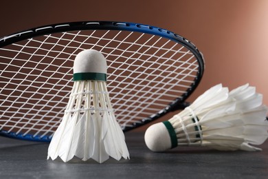 Feather badminton shuttlecocks and racket on grey table against brown background, closeup