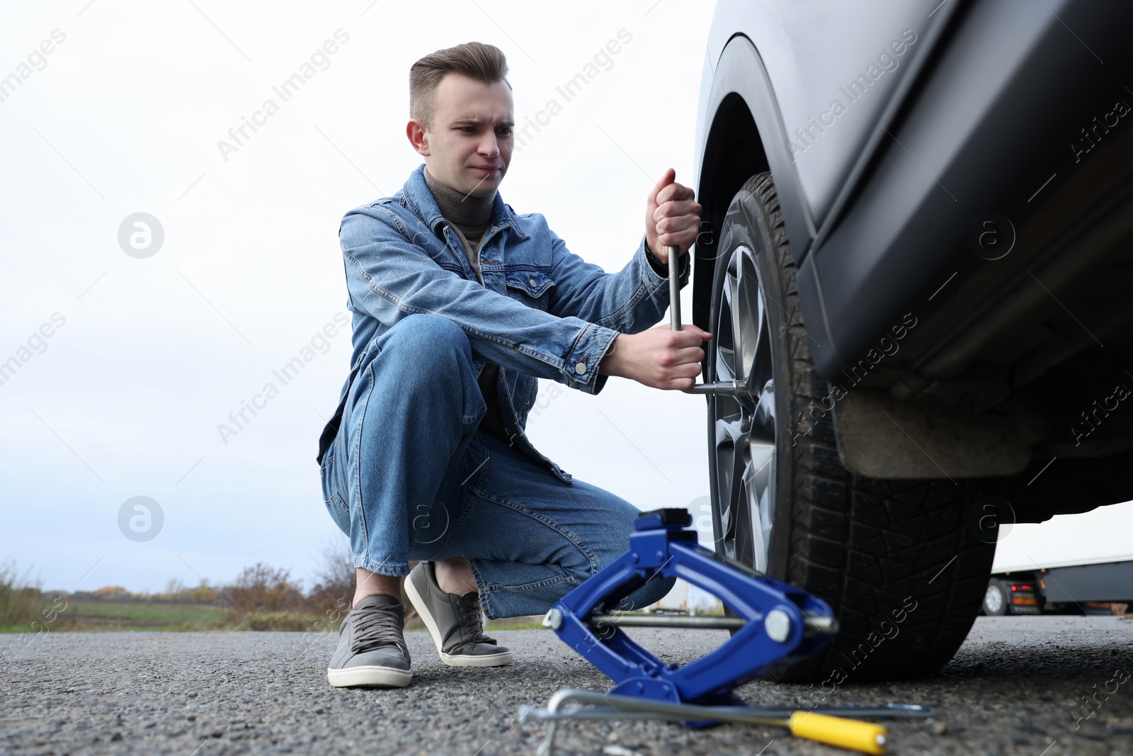 Photo of Young man changing tire of car on roadside