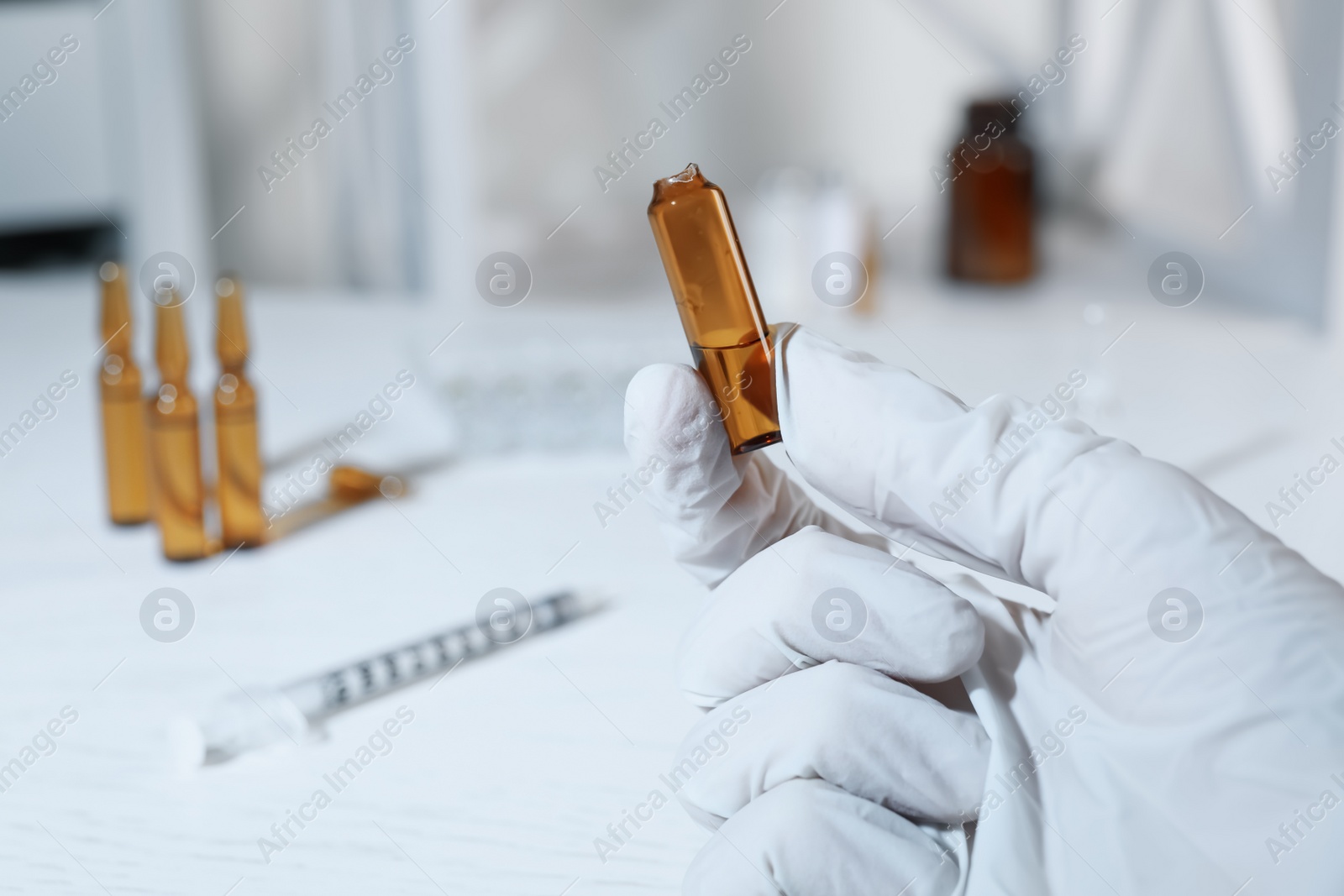 Photo of Doctor holding open pharmaceutical ampoule with medication at white table, closeup. Space for text
