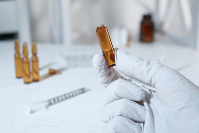 Doctor holding open pharmaceutical ampoule with medication at white table, closeup. Space for text