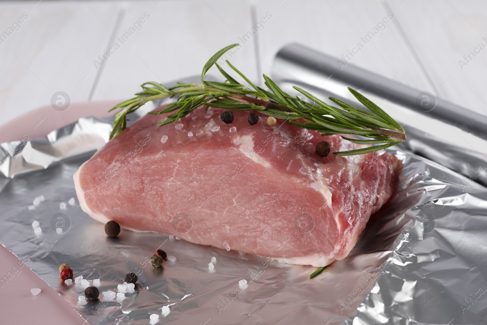 Photo of Aluminum foil with raw meat, rosemary and spices on white table, closeup