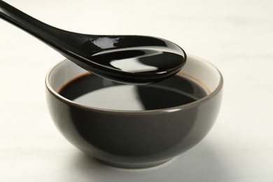 Photo of Taking soy sauce with spoon from bowl at white table, closeup