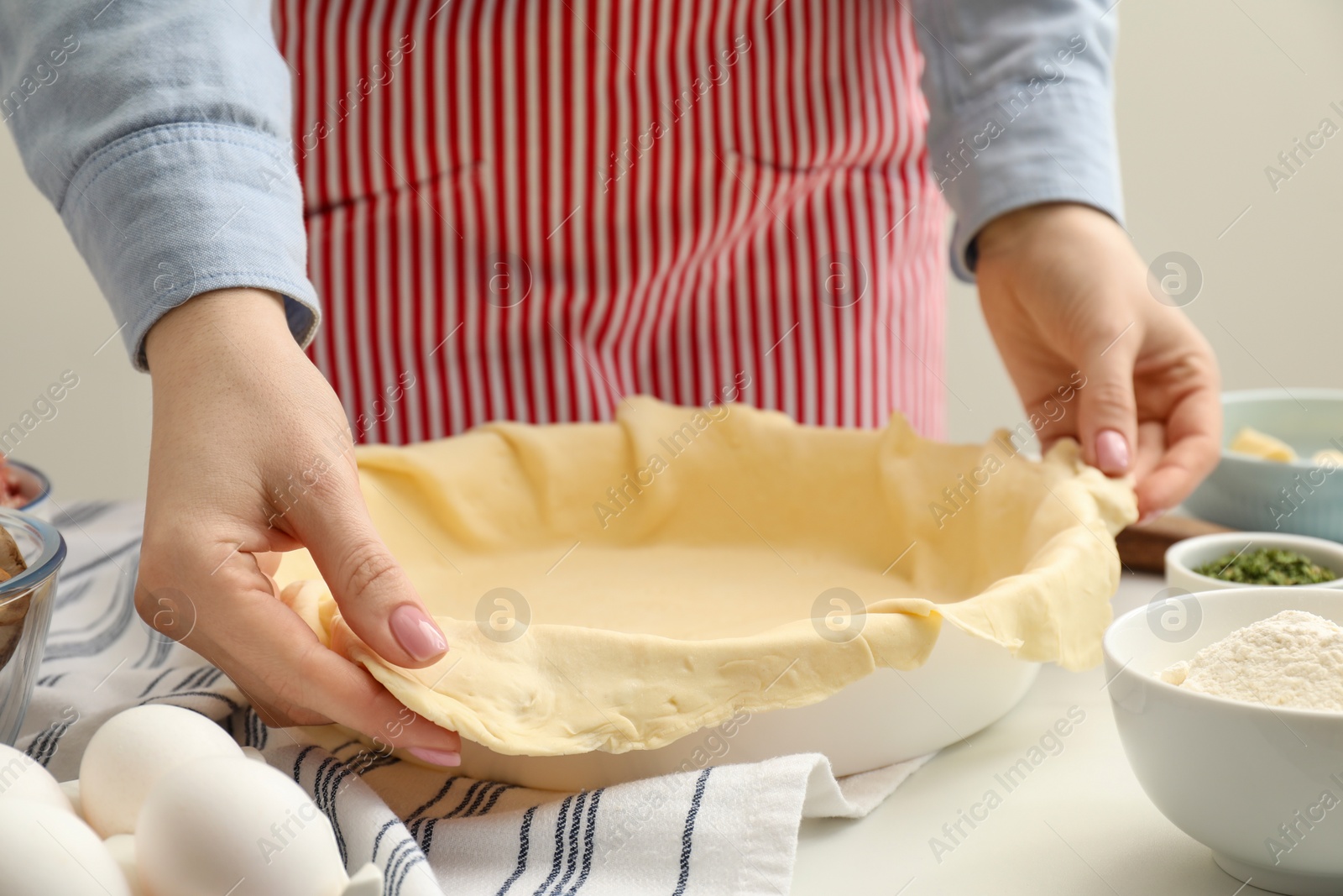 Photo of Woman putting dough for meat pie into baking dish at white table, closeup