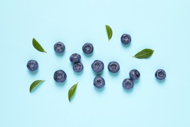 Photo of Tasty fresh blueberries with green leaves on light blue background, flat lay