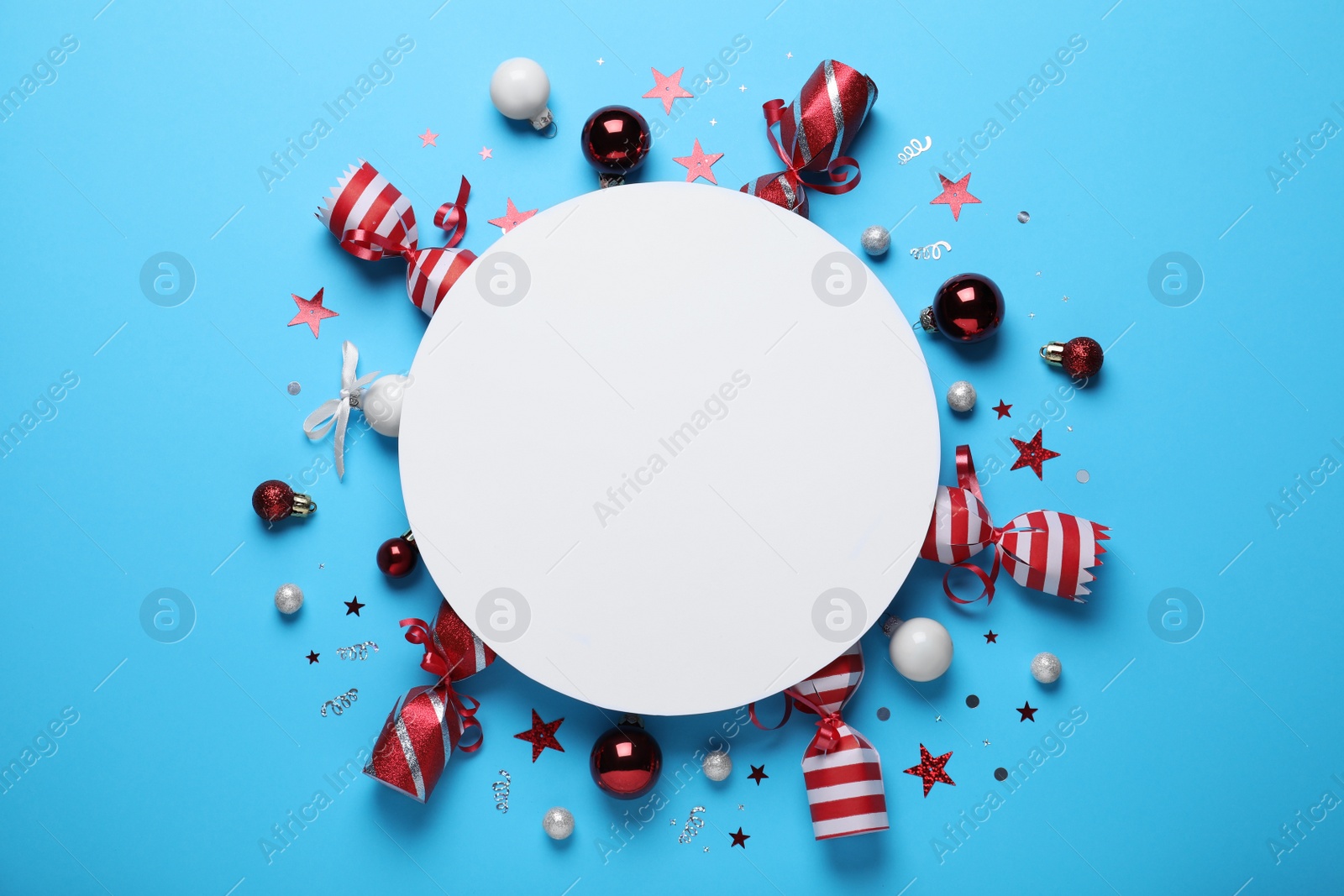 Photo of Flat lay composition of Christmas crackers, decorations, shiny confetti and blank paper on light blue background. Space for text