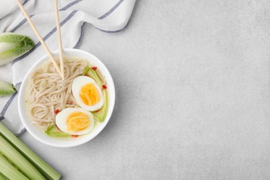Photo of Bowl of delicious rice noodle soup with celery and egg on light grey table, flat lay. Space for text