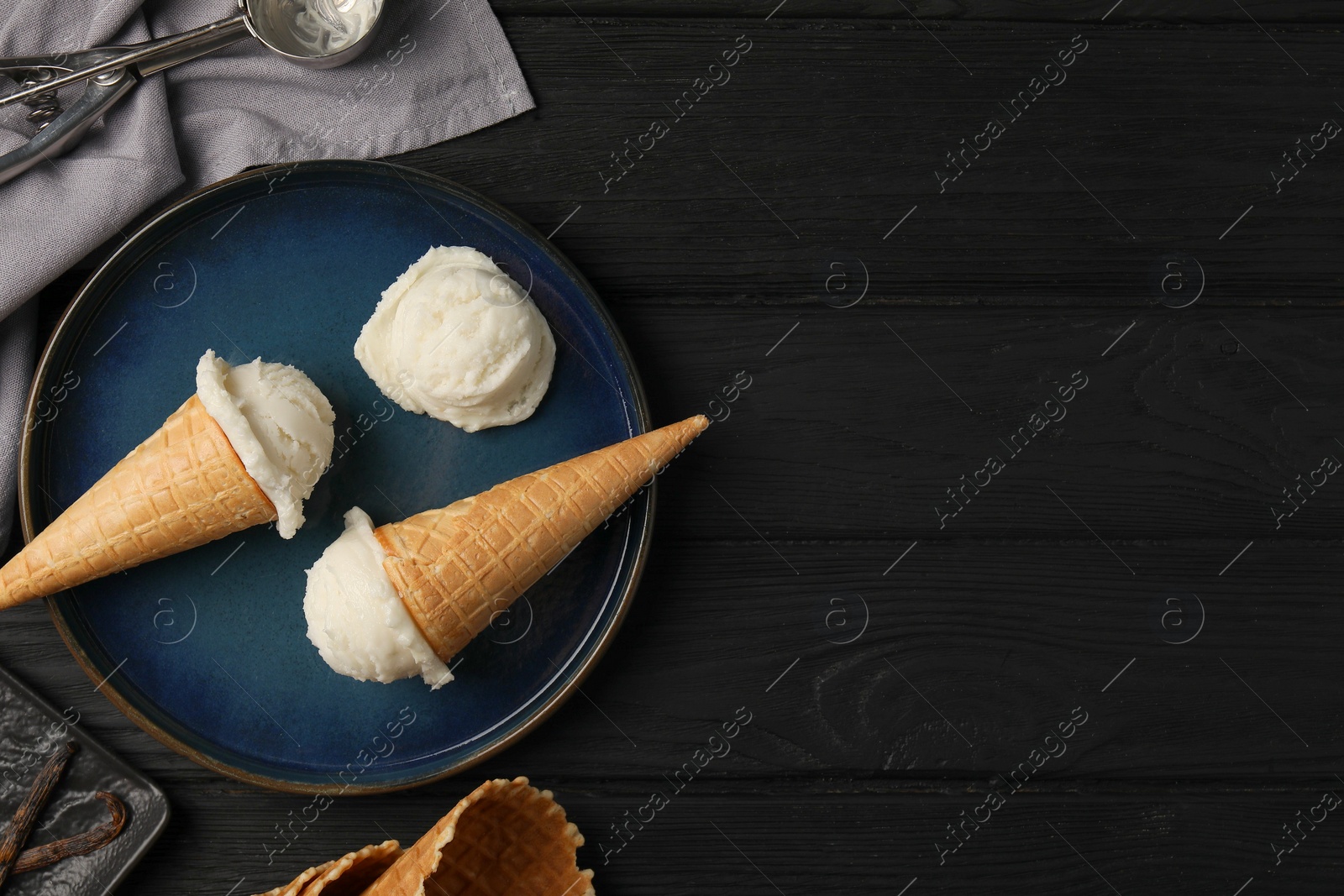 Photo of Ice cream scoops in wafer cones on black wooden table, flat lay. Space for text