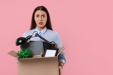 Photo of Unemployment problem. Confused woman with box of personal office belongings on pink background, space for text