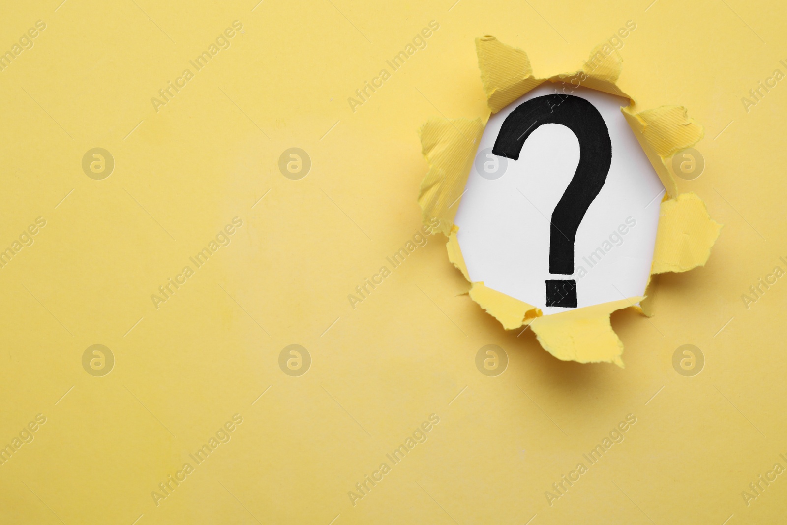 Photo of Question mark on white background, view through hole in yellow paper, space for text