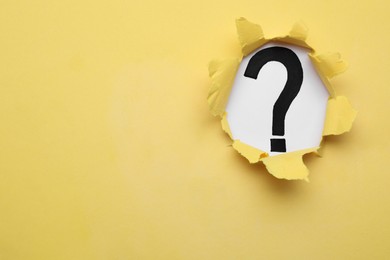 Photo of Question mark on white background, view through hole in yellow paper, space for text