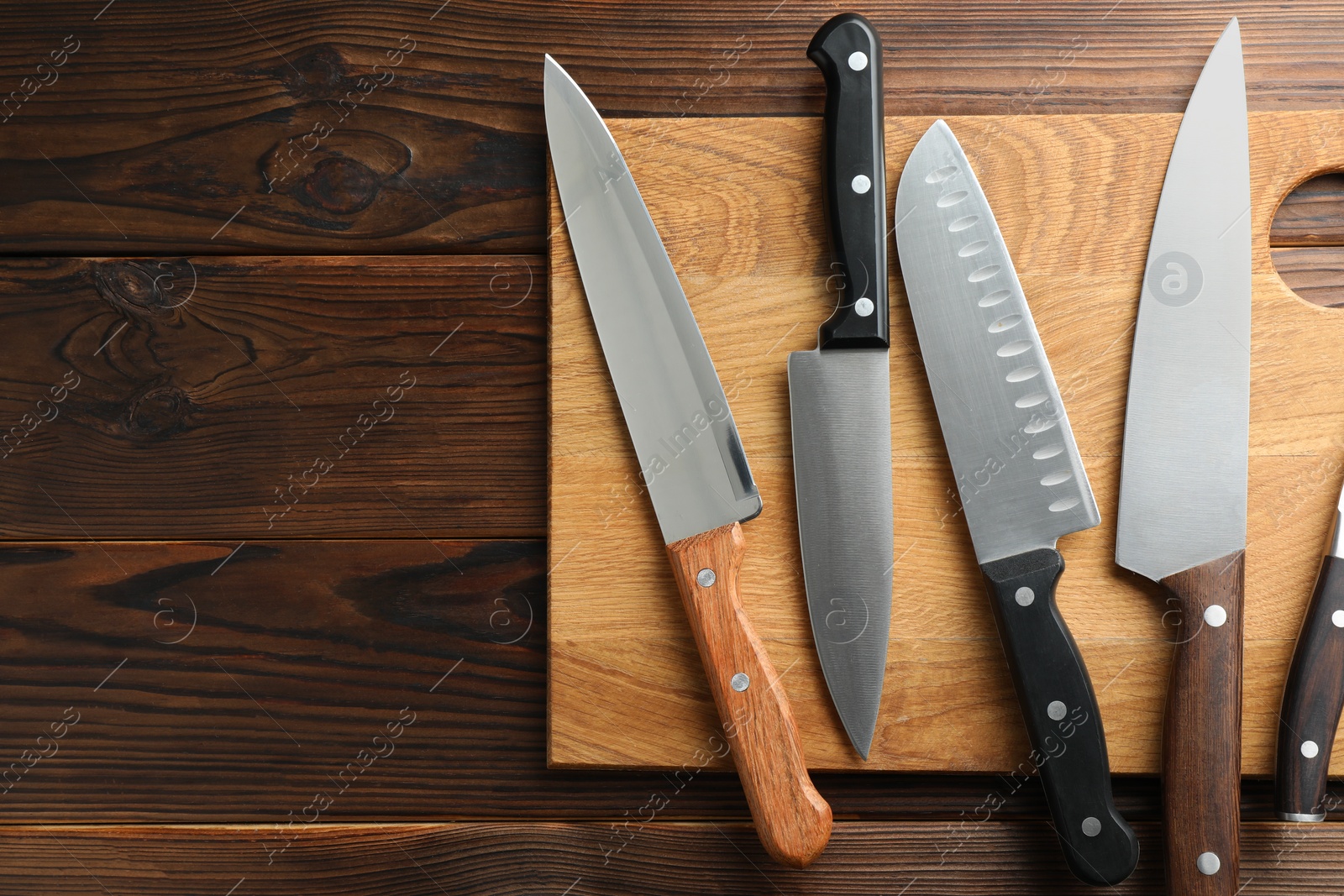 Photo of Many different knives and board on wooden table, top view. Space for text