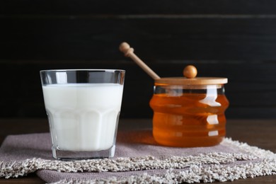 Photo of Glass of fresh milk and jar with honey on wooden table