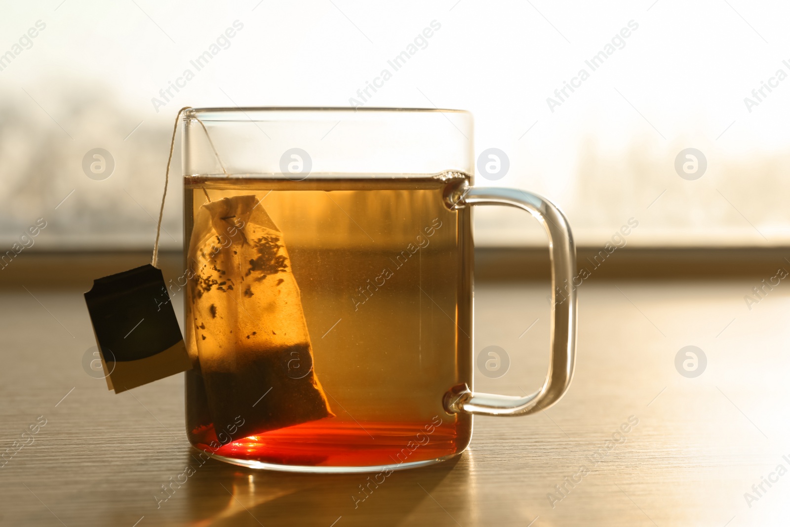 Photo of Tea bag in cup of hot water on wooden table