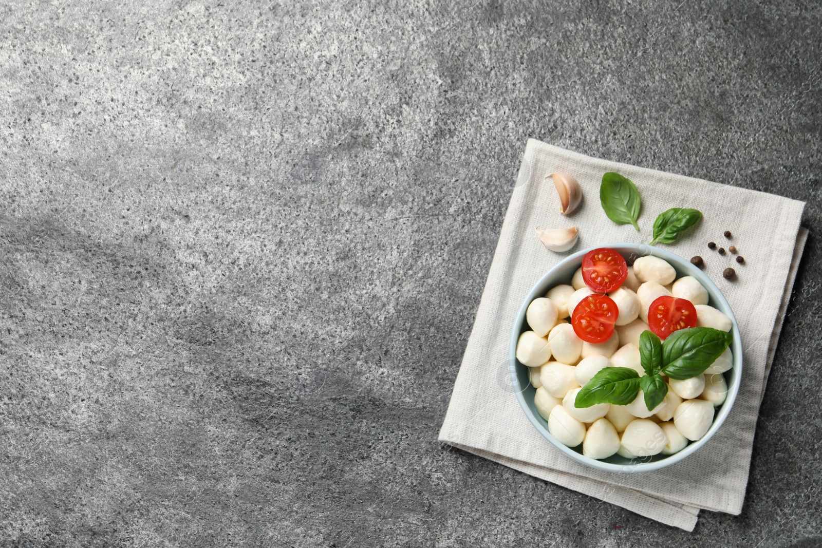 Photo of Delicious mozzarella balls with tomatoes and basil leaves on light gray textured table, flat lay. Space for text