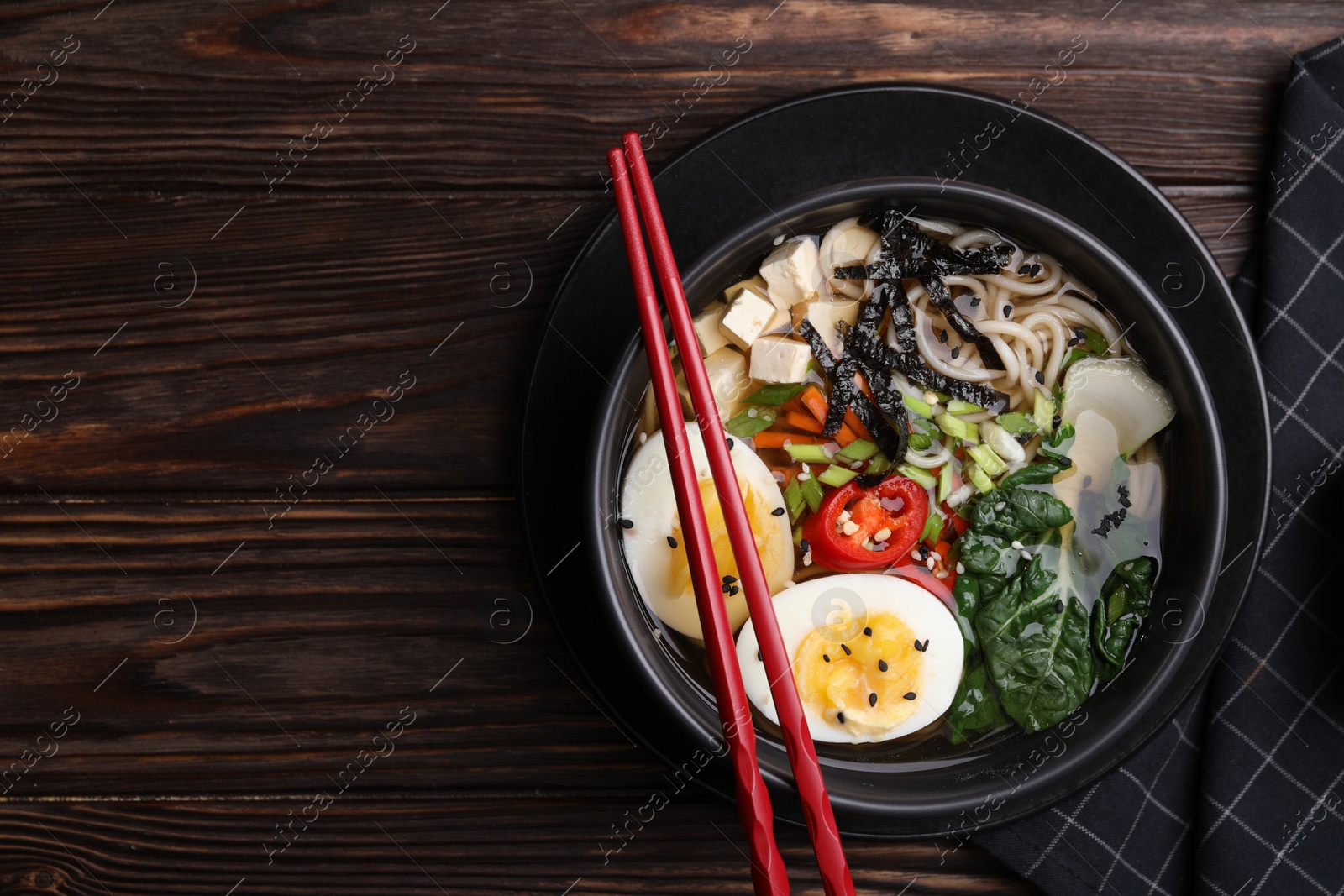 Photo of Delicious vegetarian ramen served on wooden table, top view with space for text. Noodle soup