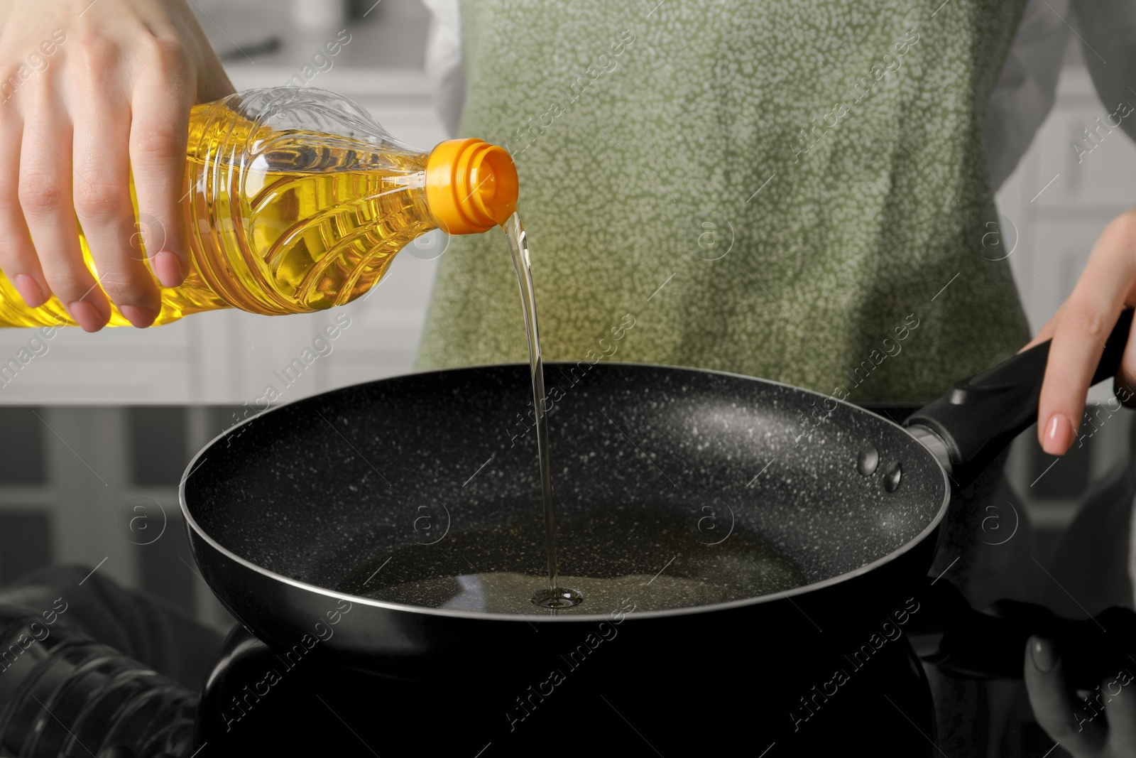 Photo of Woman pouring cooking oil from bottle into frying pan on stove, closeup