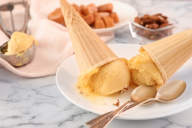 Photo of Plate with delicious yellow ice cream in wafer cones and spoons on white marble table, closeup