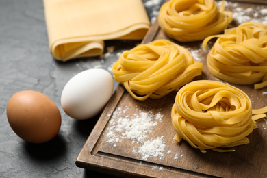 Raw tagliatelle pasta and products on black table, closeup