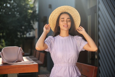 Beautiful young woman in stylish violet dress and straw hat outdoors