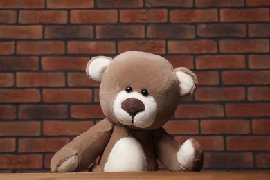 Cute teddy bear near wooden table against brick wall