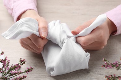 Photo of Furoshiki technique. Woman wrapping gift in white fabric at wooden table, closeup
