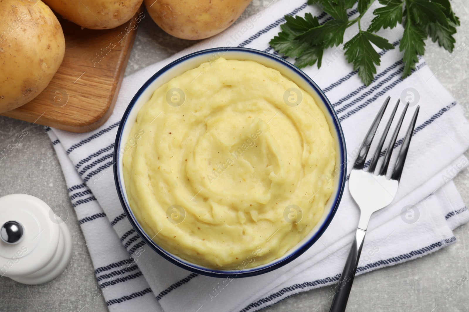 Photo of Bowl of tasty mashed potatoes served on grey table, flat lay