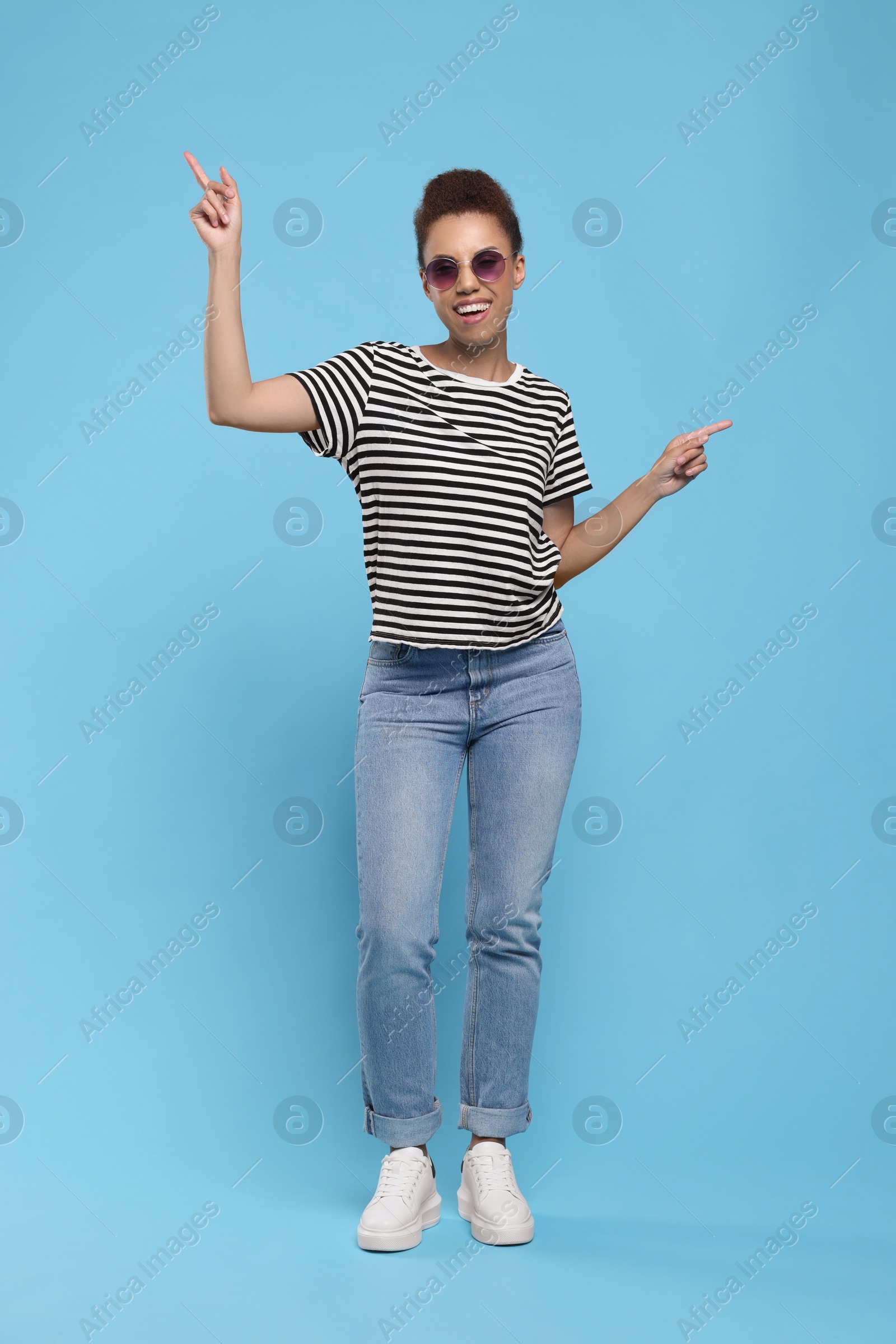 Photo of Happy young woman in stylish sunglasses dancing on light blue background