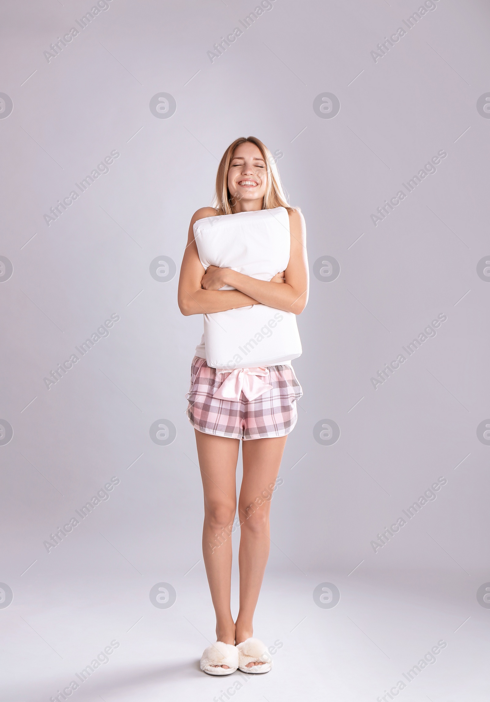 Photo of Young woman in pajamas embracing pillow on gray background