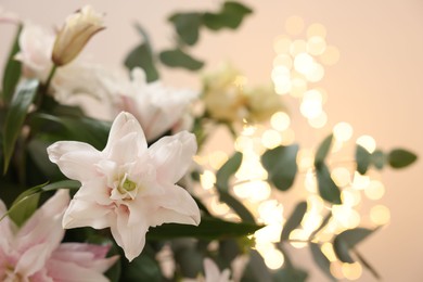 Photo of Bouquet of beautiful lily flowers against beige background with blurred lights, closeup. Space for text