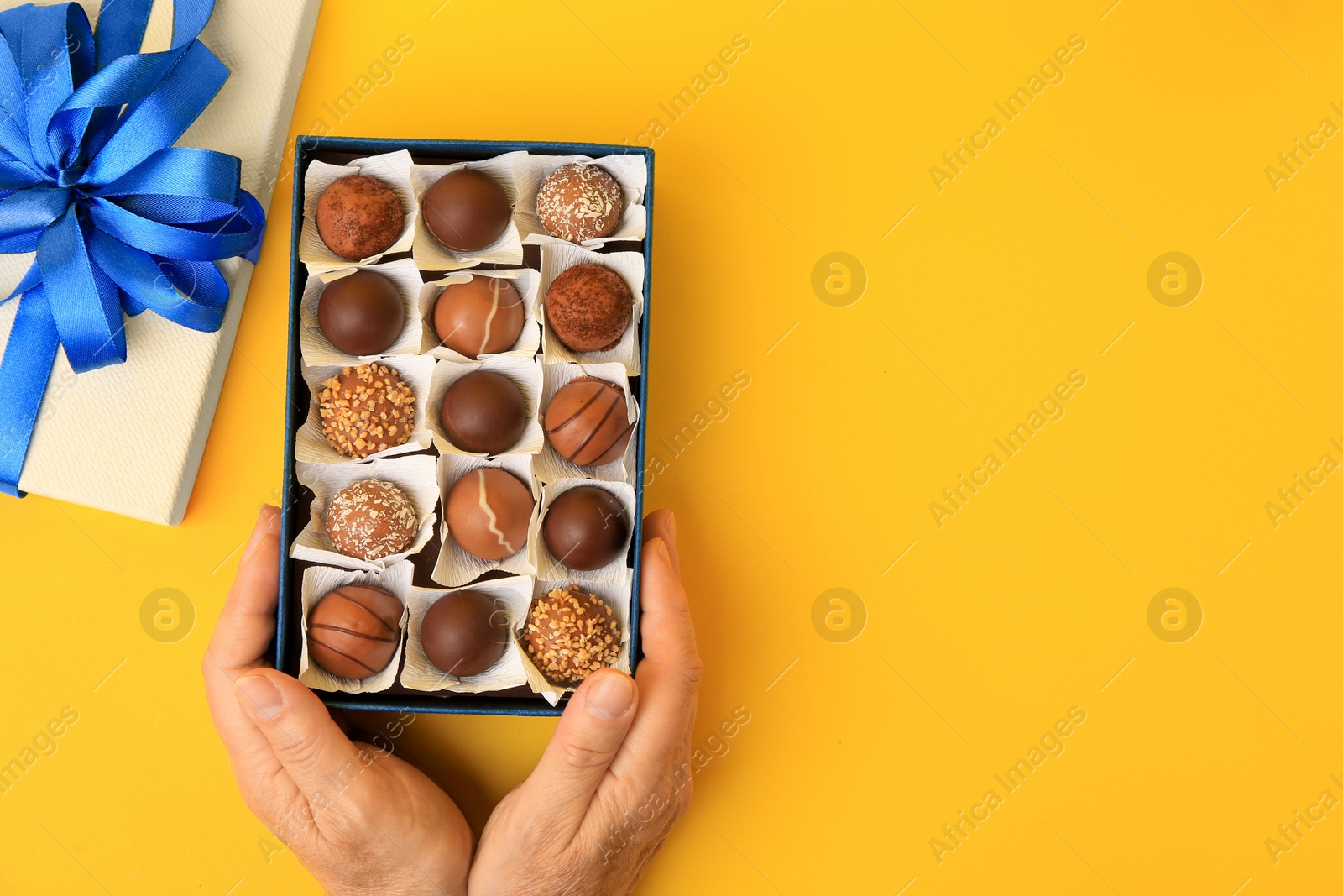 Photo of Woman with box of delicious chocolate candies on yellow background, top view. Space for text