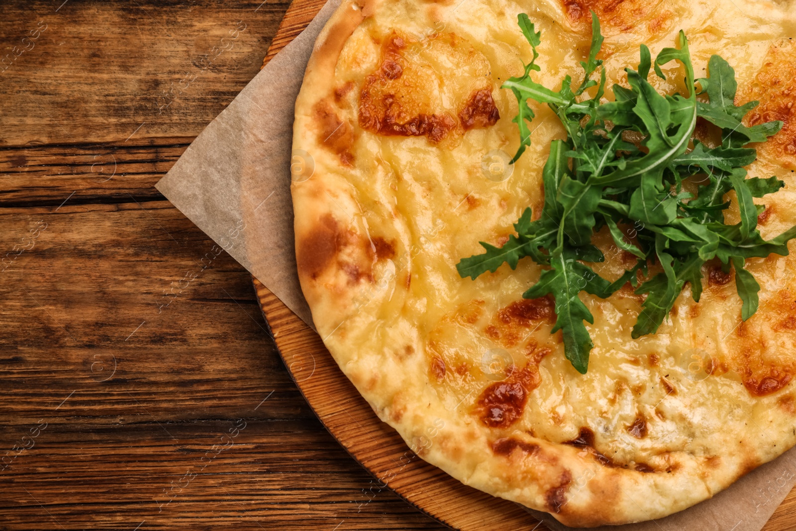 Photo of Top view of delicious khachapuri with cheese and arugula on wooden table, top view