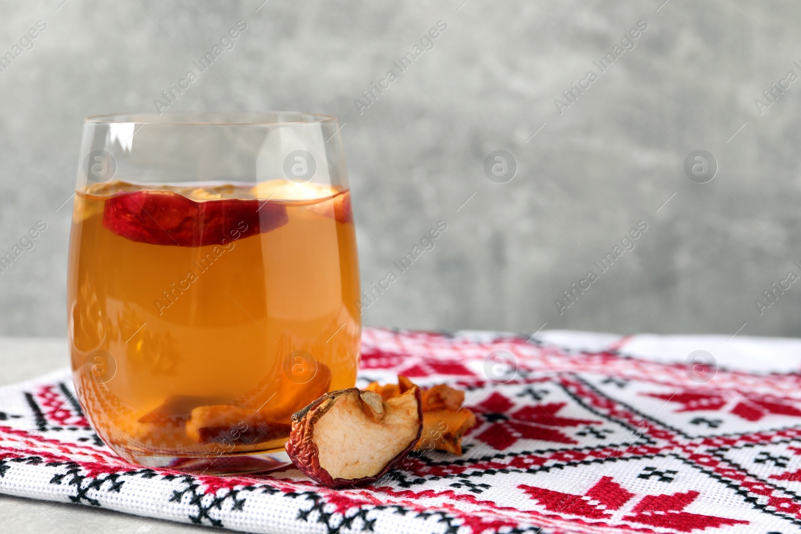 Photo of Delicious compote with dried apple slices in glass and rushnyk on table. Space for text