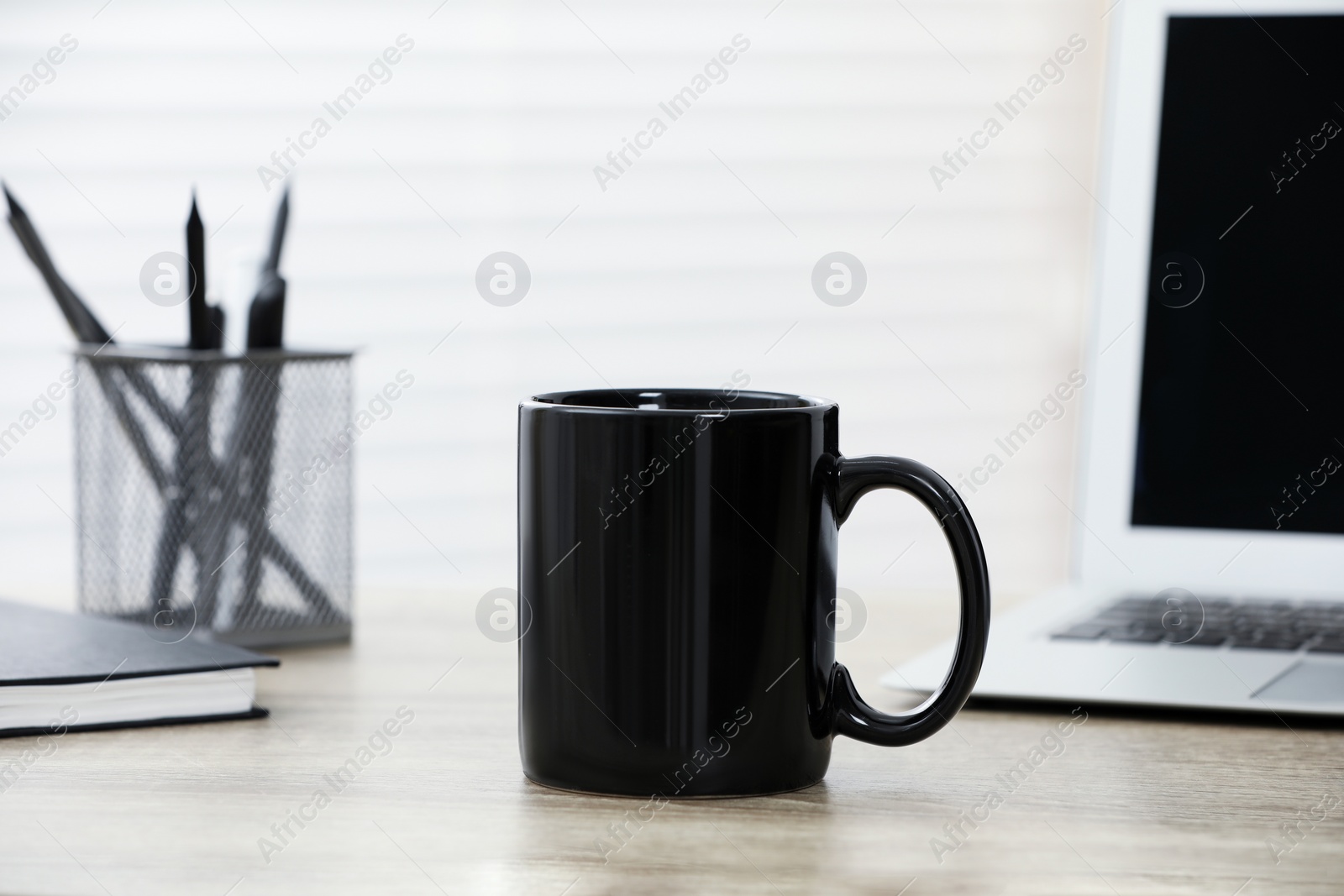 Photo of Black ceramic mug and laptop on wooden table indoors. Space for text