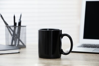 Black ceramic mug and laptop on wooden table indoors. Space for text