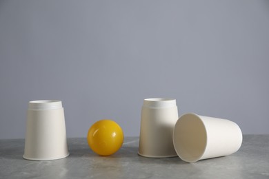 Photo of Shell game. Three paper cups and ball on grey marble table